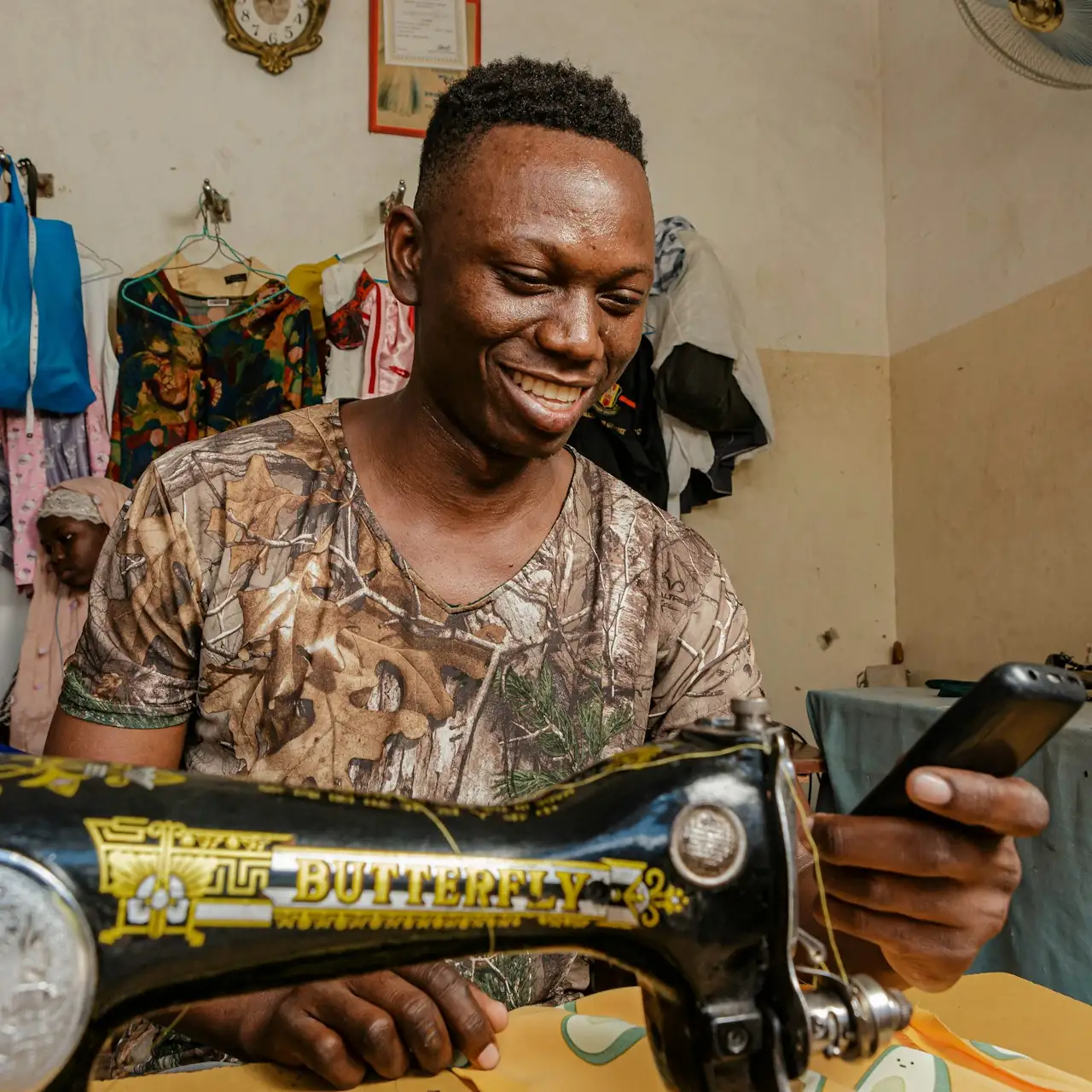 A tailor smiling at his phone beside his sewing machine